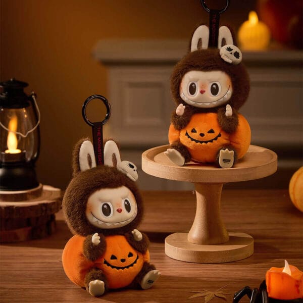 The Labubu Sitting Pumpkin plush pendant attached to the zipper of a black backpack